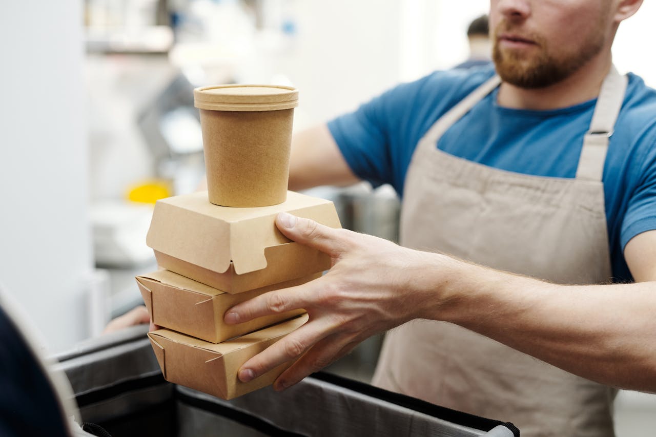 Home Man wearing apron stacks eco-friendly food containers for takeaway delivery in a kitchen setting.
